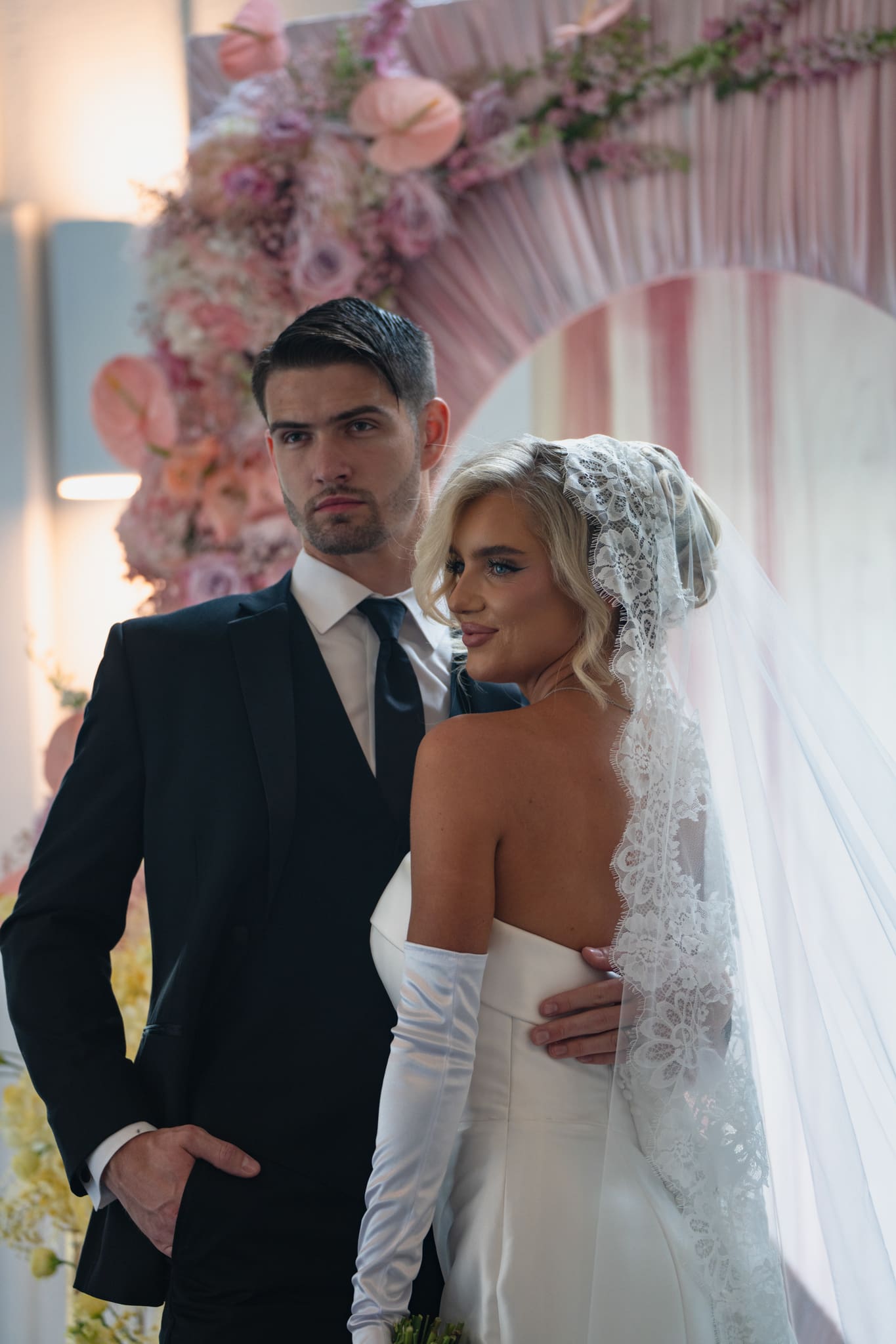 Groom holding his bride’s waist during a colorful Iowa wedding ceremony with pink, blue, and yellow floral arrangements at the altar