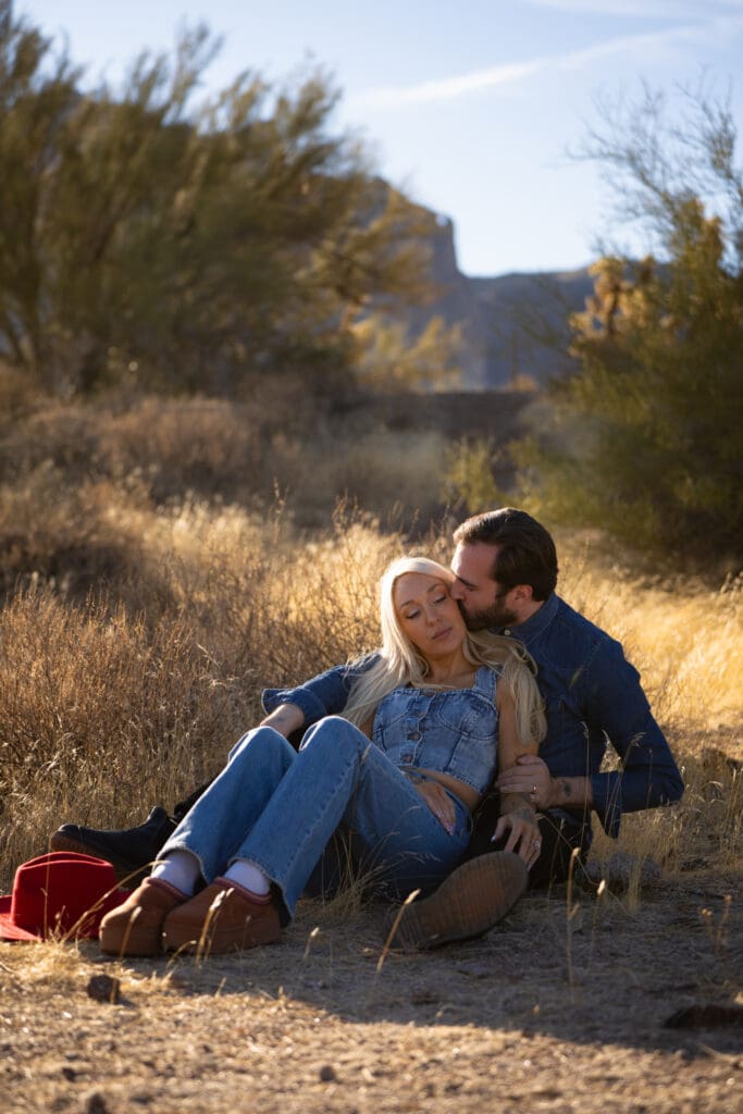 Couple sitting together in the Arizona desert holding each other as he kisses her cheek during an intimate elopement