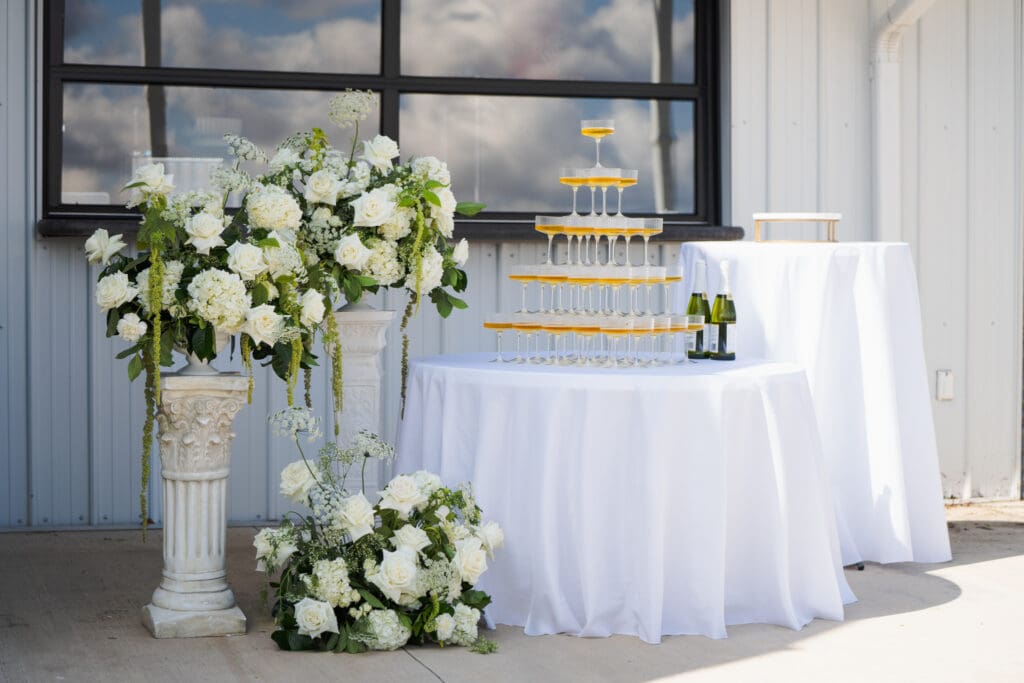 Champagne tower display at a wedding venue surrounded by elegant white floral arrangements during the reception