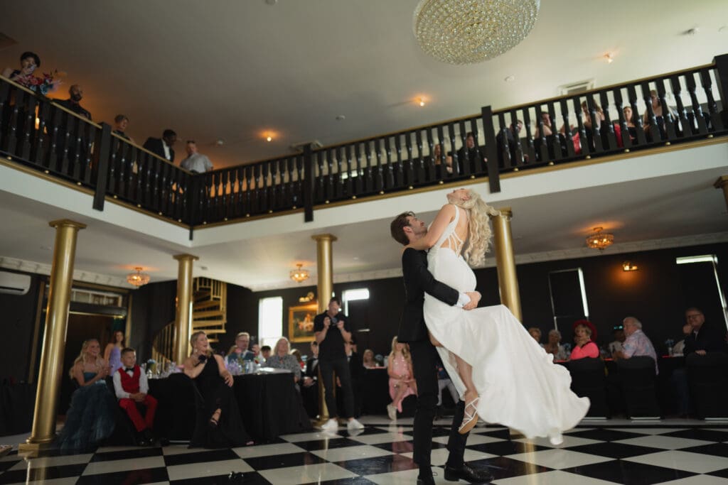 Bride being picked up and spun on the checkered dance floor at The Prelude Wedding Venue in Iowa, surrounded by family and friends during the reception